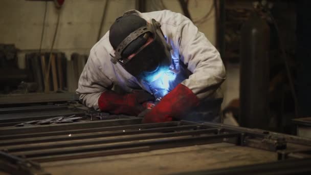 Gasschweißer steht in einer Fabrik, lehnt sich über Metallträger und schweißt - Filmmaterial, Video
