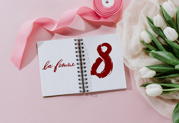 pohled shora Le Femme přihlásit Poznámkový blok, růžovou stuhou a bílými tulipány pro mezinárodní ženy den - Fotografie, Obrázek