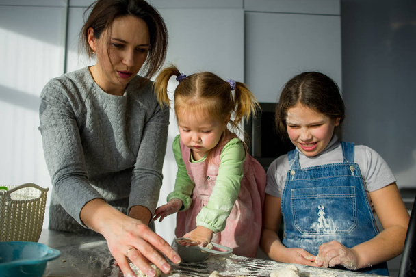 Mom teaches two little daughters to cook from dough. - Photo, Image