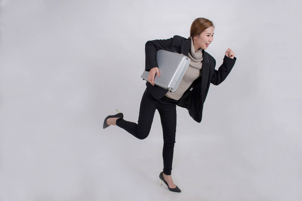Portrait of Asian business woman holding an aluminum briefcase in a hurry rushing and running over grey background - Φωτογραφία, εικόνα