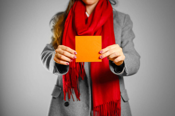 Dziewczyna w płaszcz szary i czerwony szalik posiada pomarańczowy czysty pusty squ - Zdjęcie, obraz