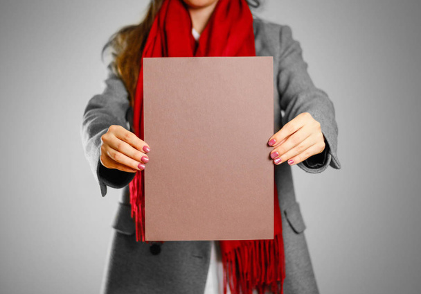 A girl in grey coat and red scarf keeps a brown clean blank shee - Foto, Imagen