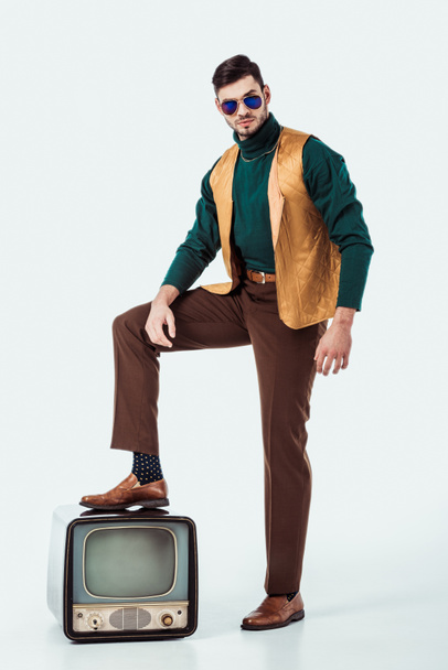 handsome retro styled man putting leg on vintage television on white - Foto, Imagem
