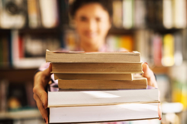 portrait of attractive happy female student holding pile of books in library  - Photo, Image