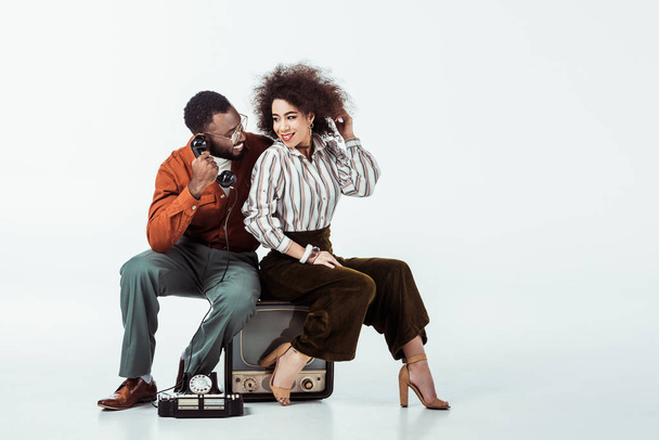 ホワイトに電話でビンテージのテレビの上に座って幸せなアフリカ系アメリカ人レトロなスタイルのカップル - 写真・画像