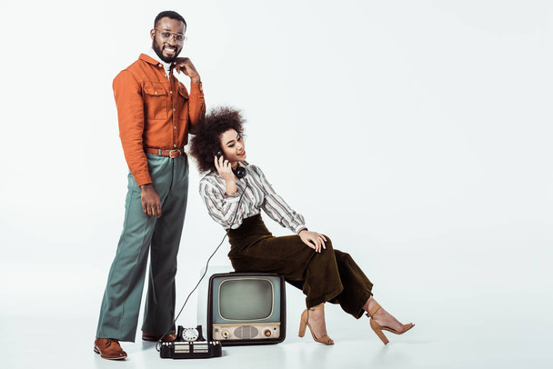 幸せなアフリカ系アメリカ人レトロなビンテージのテレビの上に座ってのガール フレンドとホワイトで電話で話していると - 写真・画像