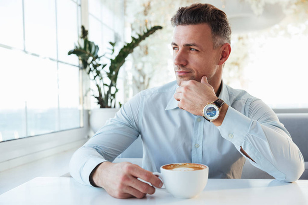 Portrait of handsome man sitting alone in city cafe with cup of  - Foto, Imagen