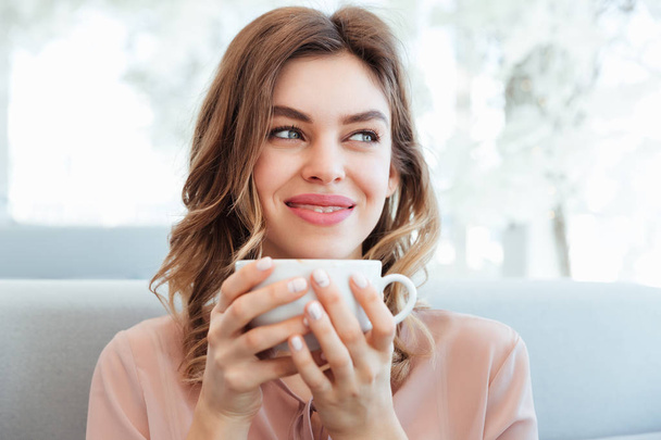 Portrait of a satisfied young woman holding cup of coffee - Фото, зображення
