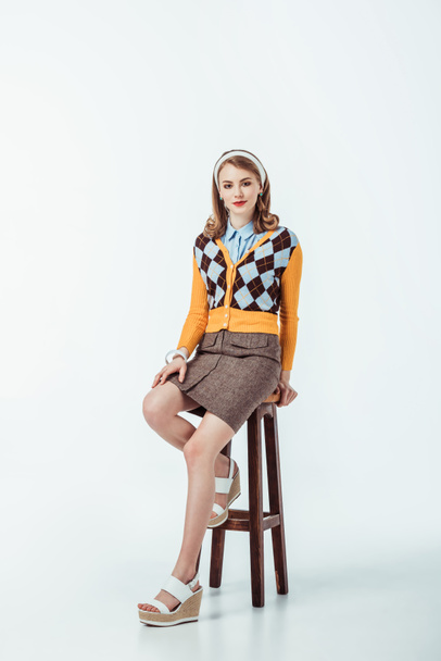 attractive retro styled girl sitting on wooden chair and looking at camera on white - Foto, afbeelding