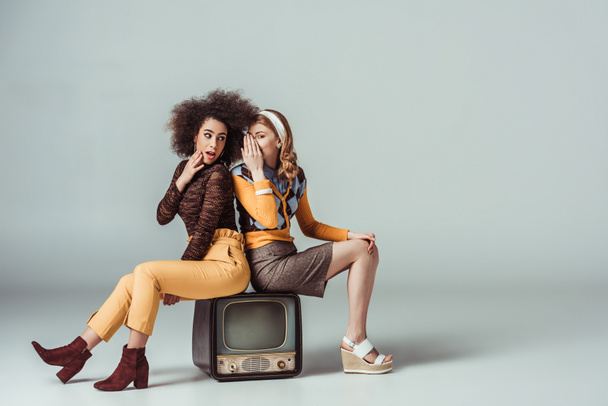 multicultural retro styled girls gossiping and sitting on vintage television - Φωτογραφία, εικόνα