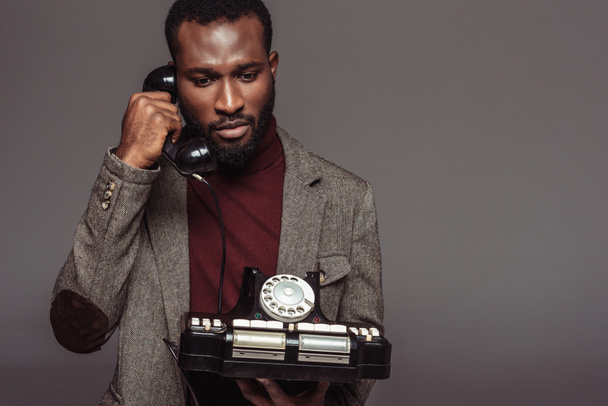 african american retro styled man talking by vintage stationary telephone isolated on grey - Photo, Image