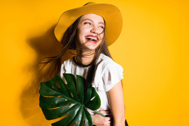 happy laughing girl model in a fashionable hat holds a green leaf, on a yellow background - Foto, Imagen