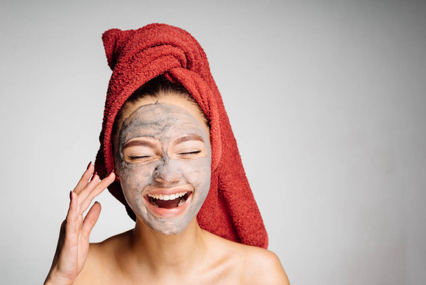 Смеющаяся молодая девушка с красным полотенцем на голове надела полезную маску для лица, дневной спа
 - Фото, изображение