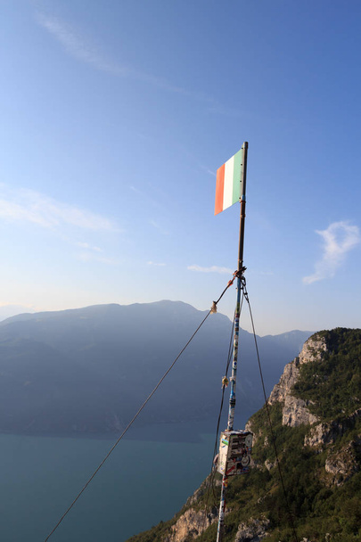 Bandera Italiana en la cumbre de la montaña Cima SAT con el Lago de Garda panorama, Italia
 - Foto, imagen