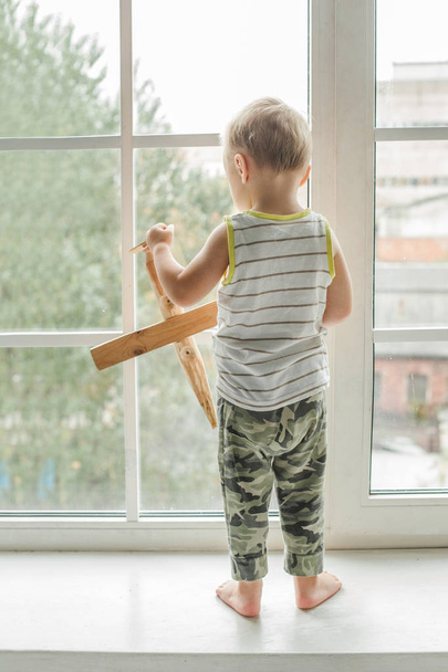 Μικρό παιδί αγόρι ψάχνει έξω το παράθυρο και αναπαραγωγή - Φωτογραφία, εικόνα