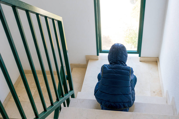 Üzgün çocuk tek başına bir merdiven köşede oturmuş - Fotoğraf, Görsel