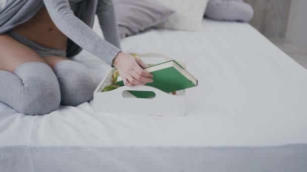 Beautiful girl in glasses sitting on bed with breakfast on tray and opens book for reading. Morning, delicious breakfast, interesting book - Záběry, video