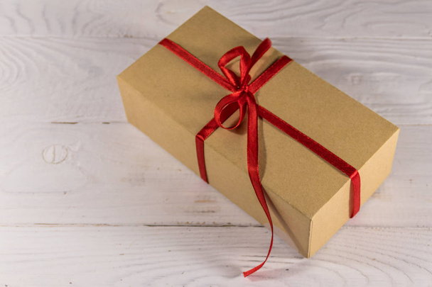 Caja de regalo de cartón con cinta roja sobre mesa de madera blanca
 - Foto, Imagen