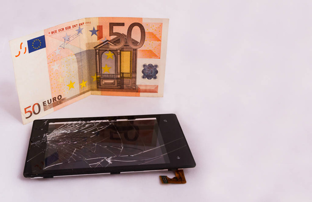 Un écran tactile cassé avec un écran et un billet en euros. isolé sur fond blanc
 - Photo, image