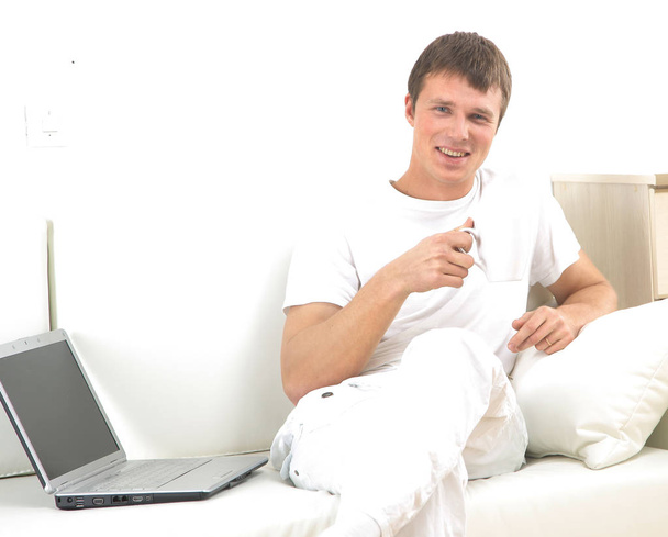 Handsome casual man sitting on couch having coffee at home. - Foto, afbeelding