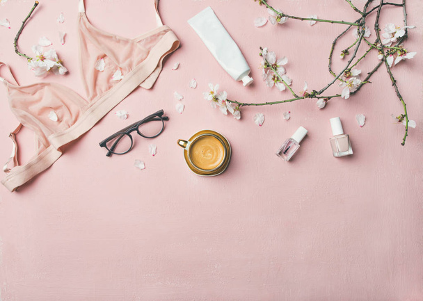 Womans morning rituals concept. Flat-lay of feminine tender powder color lingerie, glasses, cosmetic items, cup of coffee and Spring blossom flowers over pastel pink bed cover, top view, copy space. - Zdjęcie, obraz