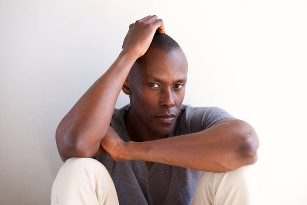 Nahaufnahme Porträt eines afrikanisch-amerikanischen Mannes, der vor einer weißen Wand sitzt und denkt - Foto, Bild