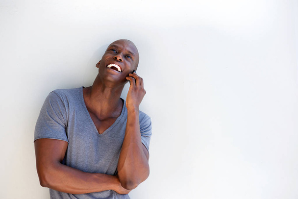 Horizontal portrait of happy black guy leaning against white background talking on cellphone - Photo, Image