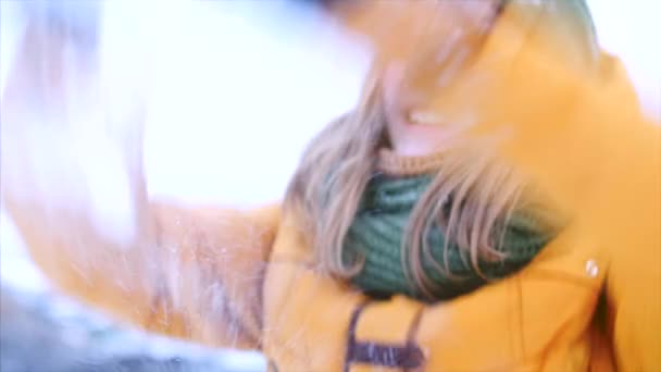 Young beautiful teenage girl teenage with blond hair, enjoying winter day outdoors, girl with a green and brown scarf in a green hipster hat, throws up the snow, looking at the camera. Slow motion - Felvétel, videó