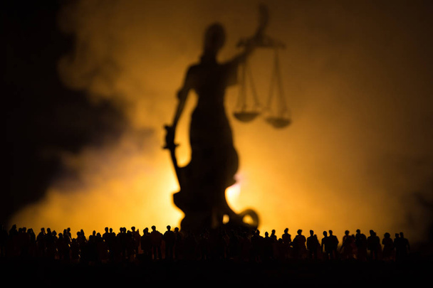 Sylwetka niewyraźne olbrzymie Pani sprawiedliwości statua z mieczem i skali stojący tłum w nocy z ognia mglisty tło. W nocy - Zdjęcie, obraz