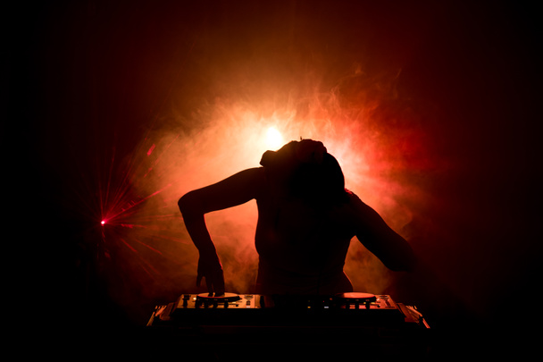 DJ spinnen, mixen en scratchen in een nachtclub, handen van dj tweaken verschillende track besturingselementen op dj's dek, strobe lights en mist, of Dj mixt de track in de discotheek op feestje - Foto, afbeelding