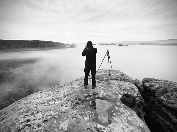 Fotograaf op de krater. Man op piek boven dikke wolk, donker regenachtig weer - Foto, afbeelding