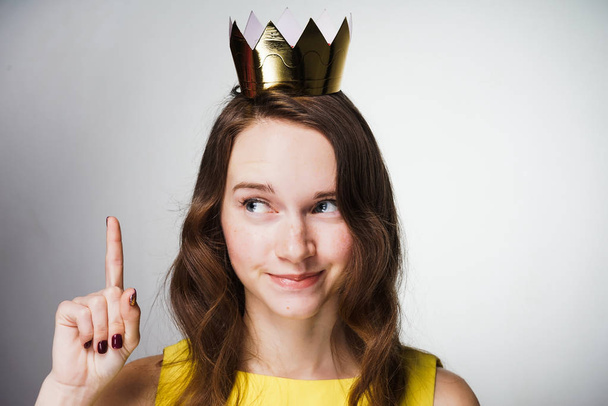 a cute young girl in a yellow dress lifted her index finger up, a golden crown on her head, an idea appeared - Photo, Image