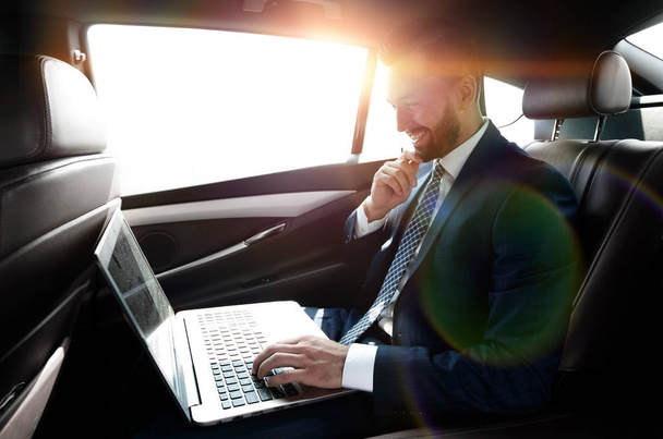 Businessman typing text on laptop while sitting in car - Фото, изображение
