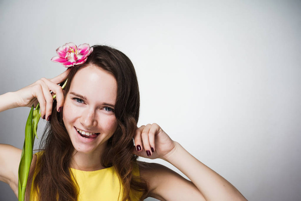 happy laughing young woman in yellow dress holds pink flower, celebrates mother's day - Foto, Imagem