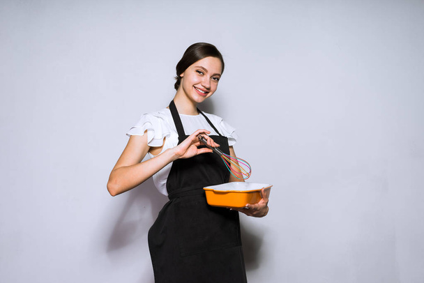 smiling young girl cook in black dress prepares a delicious dish - Photo, image
