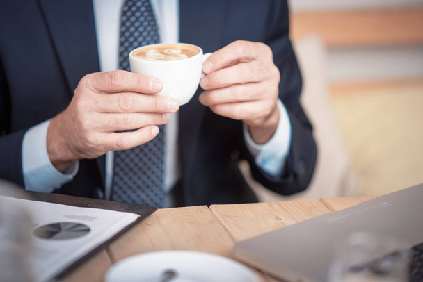 Homem de negócios maduro sênior que toma um café em uma cafeteria, revisando gráficos e gráficos
 - Foto, Imagem