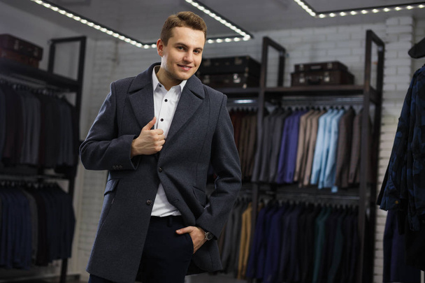 Young handsome man in coat in suit shop - Фото, изображение