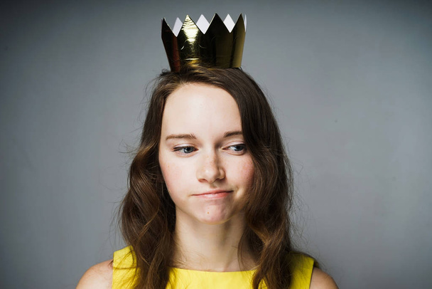 a pensive young girl in a yellow dress is waiting for Mother's Day, on her head is a golden crown - Foto, Imagem