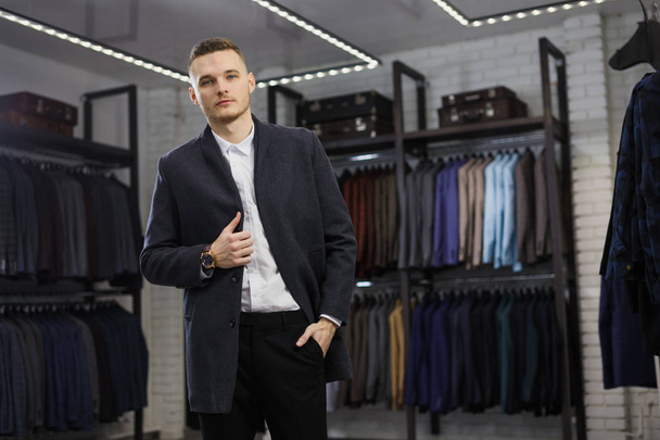 Handsome man stands in suit shop fashionable rich male dressed in expensive clothes posing indoors - Fotó, kép