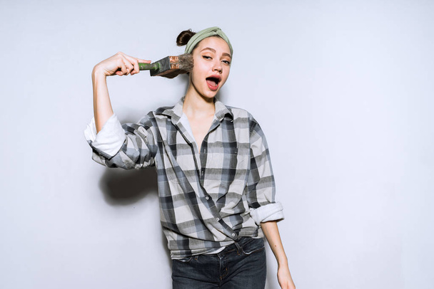 funny young girl in plaid shirt holding brush for painting walls - Photo, Image