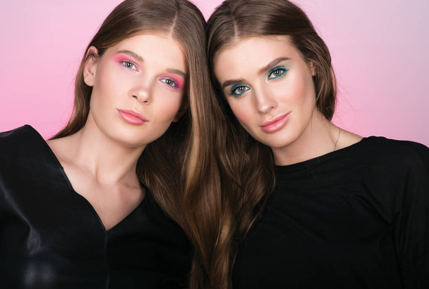 Portrait of two beautiful young women with long wavy hair. Professional makeup and black clothes - Zdjęcie, obraz