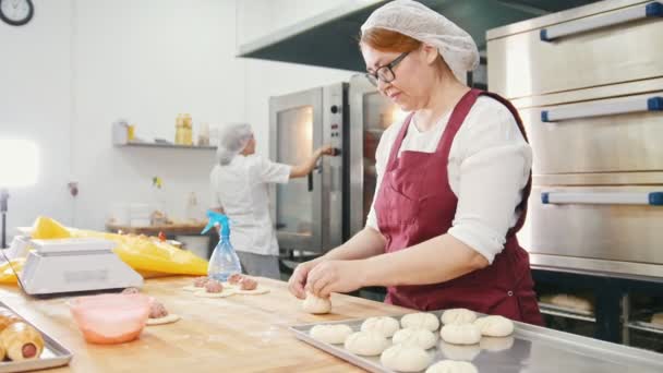 Vrouw in glazen en schort bakt taarten in de bakkerij - Video