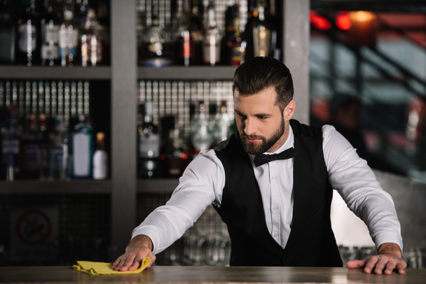 handsome bartender cleaning bar counter in evening - Foto, afbeelding