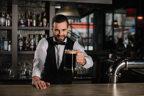 uśmiechający się przystojny barman trzymając szklankę piwa - Zdjęcie, obraz