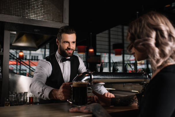 smiling handsome bartender giving glass of beer to female visitor - Photo, Image
