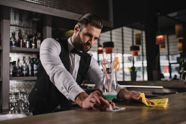 handsome bartender cleaning bar counter with rag - Foto, Imagen