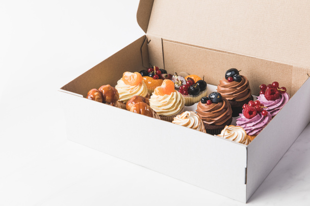 vista de cerca de varios tipos de cupcakes en caja de cartón aislado en blanco
 - Foto, Imagen