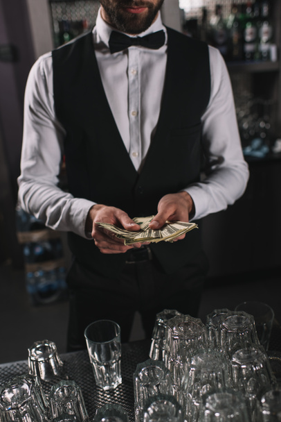 bijgesneden afbeelding van barman tellen tips bij toog - Foto, afbeelding