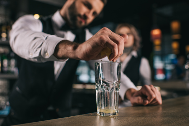 męski barman wyciskając sok z cytryny do kieliszka w barze - Zdjęcie, obraz