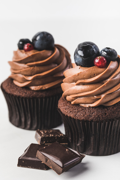 close up view of chocolate cupcakes with cream, grape, berries and pieces of chocolate isolated on white - Photo, Image